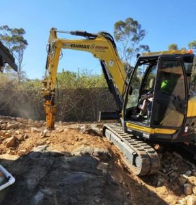 A excavator with hammer attachment braking up concrete.